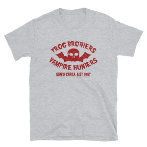 May include: Gray short-sleeved t-shirt with a red graphic print of a skull with bat wings and the text "Frog Brothers Vampire Hunters Santa Carla Est. 1987".
