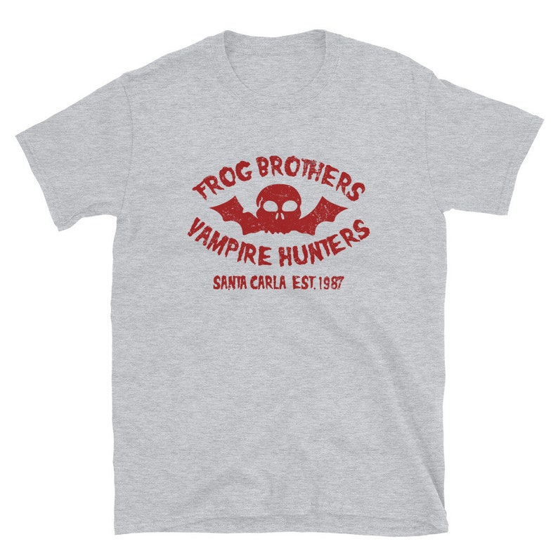 May include: Gray short-sleeved t-shirt with a red graphic print of a skull with bat wings and the text "Frog Brothers Vampire Hunters Santa Carla Est. 1987".