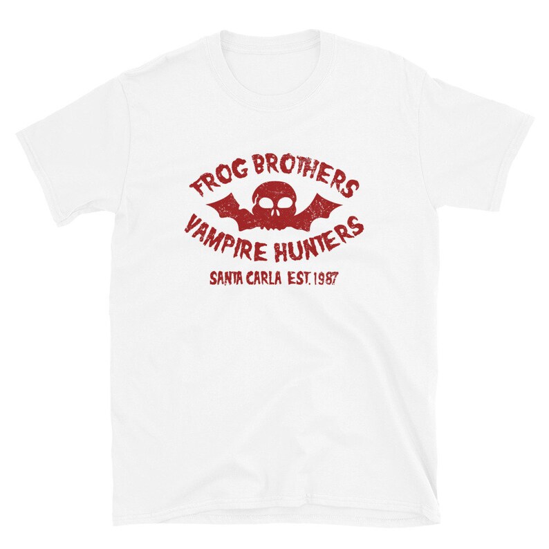 May include: White t-shirt with a red vintage-style logo that says "Frog Brothers Vampire Hunters Santa Carla Est. 1987". The logo features a skull with bat wings.