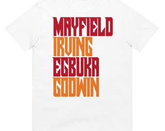 May include: A white short-sleeved t-shirt featuring a vertical graphic print of four names stacked in alternating red and orange block lettering. The names printed on the front of the shirt are MAYFIELD, IRVING, EGBUKA, and GODWIN in a bold font.