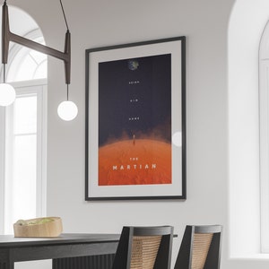 May include: A black framed poster with a red and blue image of a person walking on Mars. The poster has the text "Bring Him Home" and "The Martian" on it.