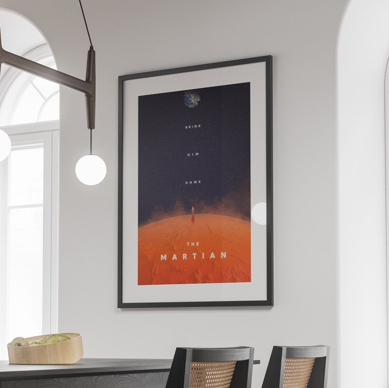 May include: A framed movie poster for the film "The Martian" featuring a red planet landscape with a lone astronaut walking towards the camera. The text "Bring Him Home" is displayed above the astronaut and "The Martian" is displayed below the astronaut.