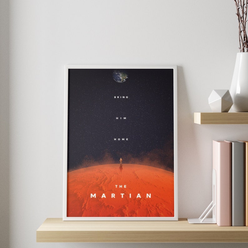 May include: A white framed poster with a black background and a red planet in the foreground. The poster features a silhouette of an astronaut standing on the planet. The text on the poster reads "Bring Him Home" and "The Martian".