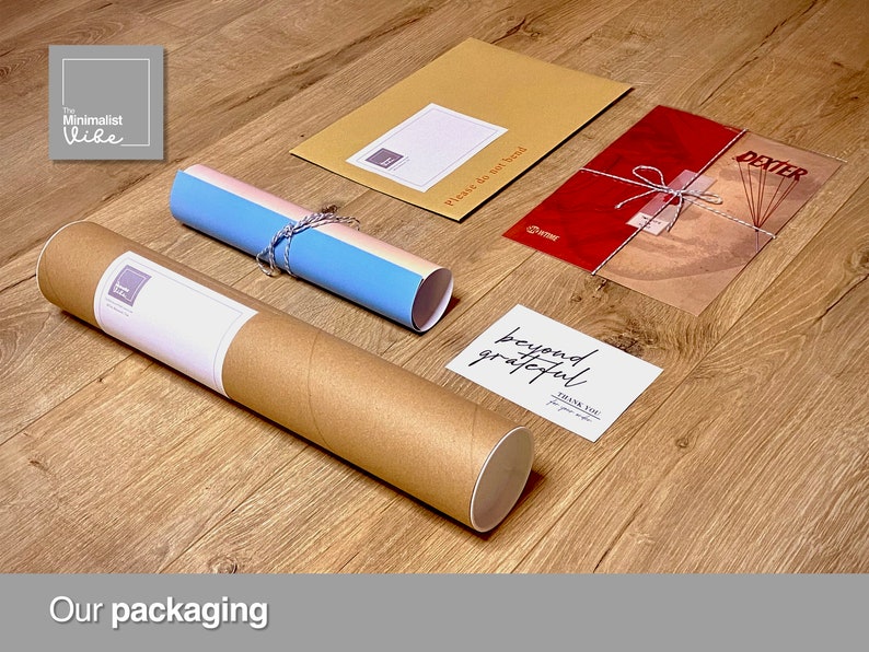 May include: A brown cardboard tube with a white label that says "The Minimalist Vibe" is used to package a rolled poster. The poster is wrapped in a blue and white paper with a string tied around it. A red envelope with a white string tied around it and a white card with the text "beyond grateful" are also included in the packaging.