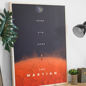 May include: A framed poster with a minimalist design featuring a red planet with a lone astronaut standing on its surface. The text "Bring Him Home" and "The Martian" are displayed on the poster.