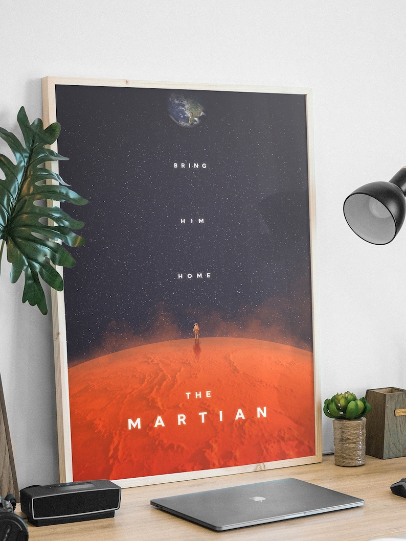 May include: A framed poster with a minimalist design featuring a red planet with a lone astronaut standing on its surface. The text "Bring Him Home" and "The Martian" are displayed on the poster.