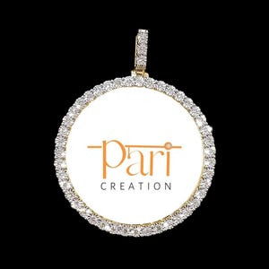 May include: A round pendant with a white background and a gold border. The pendant is set with small diamonds and features the text "pari CREATION" in orange.