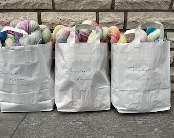 May include: Three white paper bags with colorful yarn inside. The bags are labeled "Deichsner's Wolltute" with different weights: 1000g, 800g, and 500g.