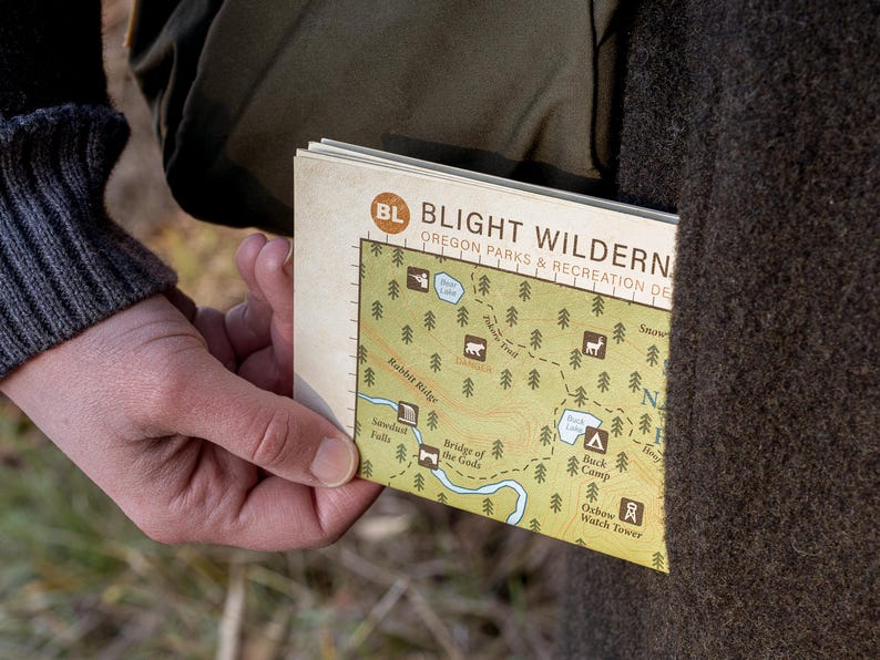 A close up shot of a folded topographical map being taken out of a coat pocket. The words "Blight Wilderness" and "Oregon Parks" can be seen, as well as some park symbols, dotted trails, and water symbols.