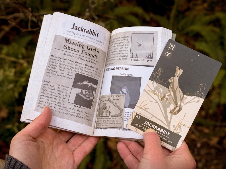 A hand holds open a book with the title "Jackrabbit" with several clippings from newspapers concerning a missing person. A card is held next the book, also titled "Jackrabbit" with an illustration of a rabbit jumping in a dark snowy setting.