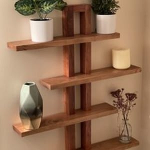 Op de afbeelding: Een set van vier houten planken met een uniek geometrisch ontwerp. De planken zijn gemaakt van donker hout en hebben een natuurlijke afwerking. De planken zijn aan een muur bevestigd en zijn versierd met planten en vazen.
