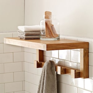 Peut inclure: Une étagère en bois avec des crochets fixés en dessous. L'étagère est montée sur un mur en carrelage blanc. Il y a des serviettes et des peignes sur l'étagère.