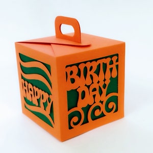 May include: Orange gift box with a handle, featuring a green cutout design with the words "Happy" and "Birthday".