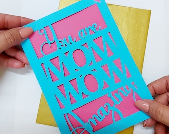 May include: A turquoise card with a pink insert. The card has a cut-out design that spells out "You are Mom Wow Amazing".