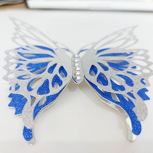 Peut inclure: Une d&eacute;coration murale en forme de papillon argent&eacute;e et bleue avec une finition scintillante. Le papillon a des d&eacute;coupes complexes et une rang&eacute;e de strass au centre.