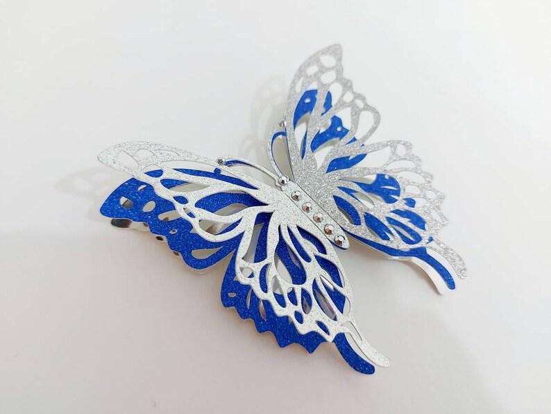 Peut inclure: Une pince &agrave; cheveux en forme de papillon avec des paillettes argent&eacute;es et bleues. Le papillon a un design d&eacute;coup&eacute; d&eacute;taill&eacute; et est accentu&eacute; de strass argent&eacute;s.
