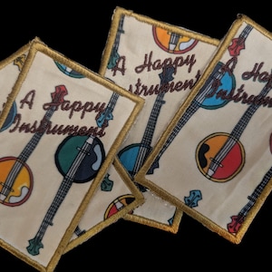 May include: Several beige fabric patches with a gold border and a banjo illustration. The text "A Happy Instrument" is embroidered on each patch. The banjo illustrations are in various colors, including blue, green, and orange.