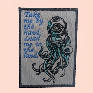 May include: Embroidered patch featuring a teal and black diver's helmet and tentacles design. The patch includes the text "Take me by the hand, Lead me to the land" in blue. The patch has a gray background and a dark gray border.