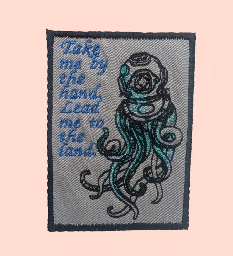 May include: Embroidered patch with a teal and black diver's helmet and tentacles design. The patch includes the text "Take me by the hand, Lead me to the land" in blue. The patch has a grey background and a dark grey border.