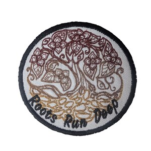 May include: Round embroidered patch featuring a tree design with flowers and leaves in shades of brown and gold. The patch has a black border and the words "Roots Run Deep" are embroidered in a curved font.