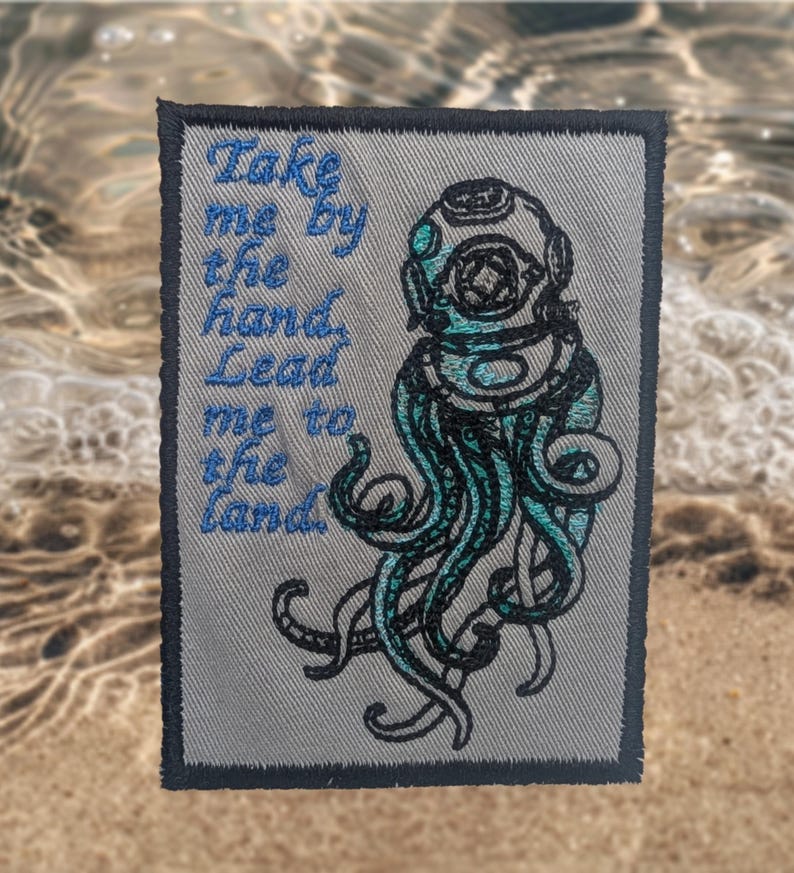 May include: A grey rectangular patch with a dark blue border. It features a teal and black illustration of a vintage diving helmet with tentacles and the text "Take me by the hand, Lead me to the land" in blue.