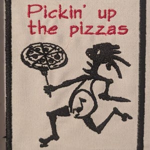 May include: Embroidered patch with the text "Pickin' up the pizzas" in red thread. A black stick figure is running while holding a pizza. The patch has a black border and is on a cream-colored background.