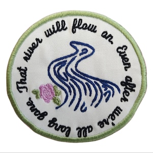 May include: Embroidered patch with a white background, featuring a blue river design and a pink rose. The patch is bordered with green stitching and includes the text "That river will flow on, even after we're all long gone."