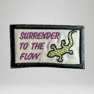 May include: Embroidered patch with the words "SURRENDER TO THE FLOW" in purple script above a green lizard. The patch has a white background with a black border.