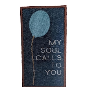 May include: Embroidered patch with a blue balloon design and the text "MY SOUL CALLS TO YOU." The patch has a denim background and a brown border. The balloon is light blue, and the text is white.