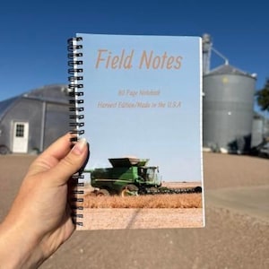 May include: A spiral-bound notebook with a light blue cover featuring a green combine harvester in a field. The text reads Field Notes, 80 Page Notebook, Harvest Edition/Made in the U.S.A. The notebook has a black wire coil binding.