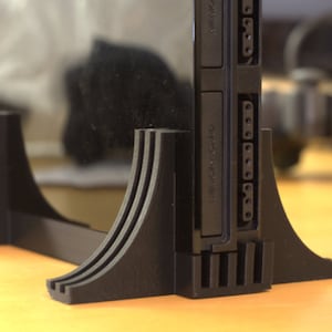 May include: A black plastic stand with a curved base and multiple slots for a video game console. The console has a black plastic case with a label that reads "MEMORY CARD" and "GAME BOY ADVANCE".