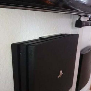 May include: Two black gaming consoles mounted on a white wall. The console on the left has a PlayStation logo.