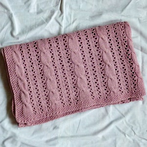 May include: A pink knitted baby blanket with a cable knit pattern.