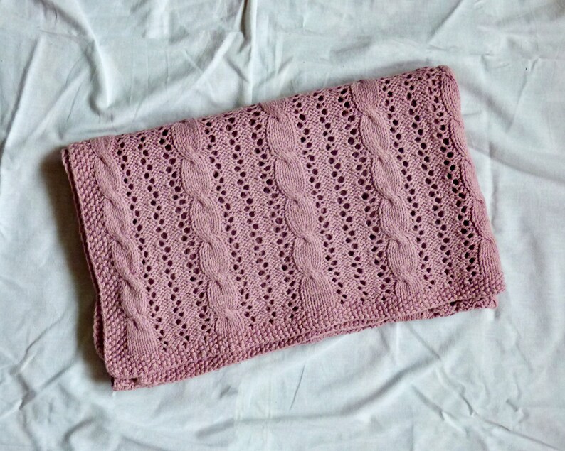 May include: A pink knitted baby blanket with a cable knit pattern.