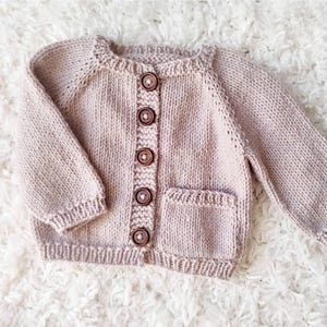 May include: A pale pink knitted cardigan with a pocket and wooden buttons.