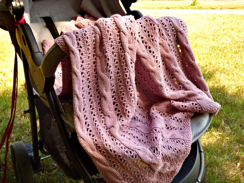 May include: A pink knitted baby blanket with a cable knit pattern, draped over a stroller.