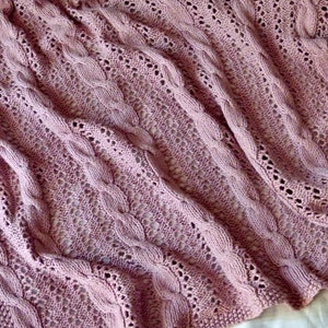 May include: A soft, pink knitted throw blanket with a cable knit pattern and openwork design.