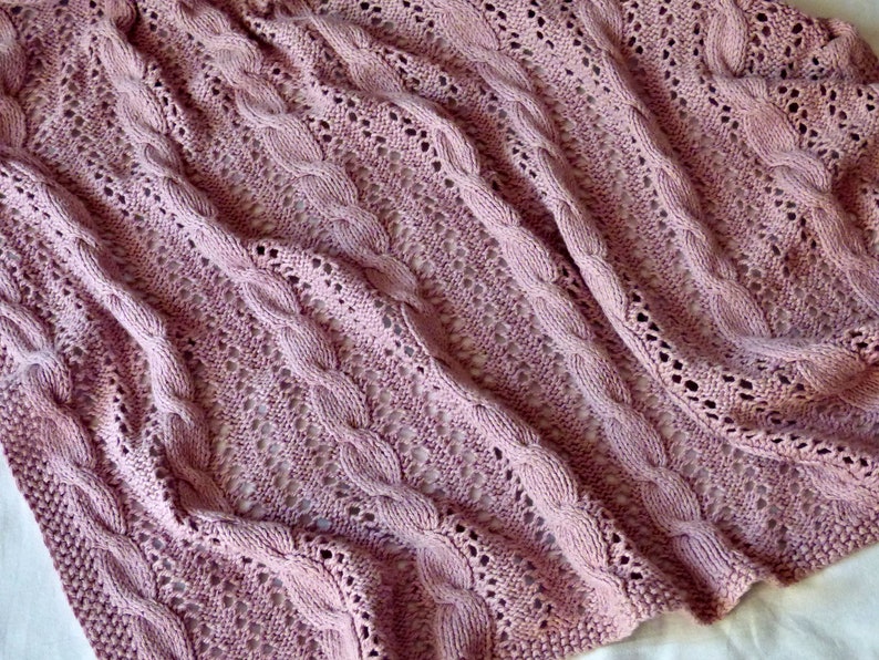 May include: A soft, pink knitted throw blanket with a cable knit pattern and openwork design.