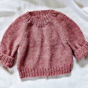 以下が含まれることがあります： 長袖でクルーネックのピンクのニットセーターです。