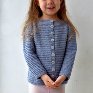 May include: A light blue knitted cardigan with a button closure. The cardigan has a ribbed texture and is worn by a young child.