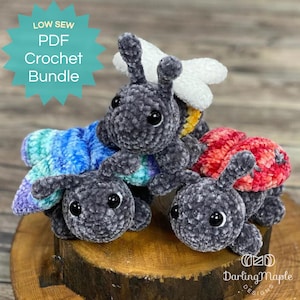 May include: A set of four crocheted amigurumi bugs, including a ladybug, a bee, and two butterflies. The bugs are made with a soft, fuzzy yarn and have large, black eyes. The bugs are sitting on a wooden surface. LOW SEW PDF Crochet Bundle.