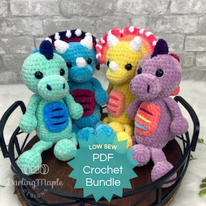 May include: A set of four crocheted dinosaur amigurumi toys in various colors, including green, blue, yellow, and purple. The toys are sitting on a black metal tray with a wooden base. The text "LOW SEW PDF Crochet Bundle" is on a teal starburst sticker.