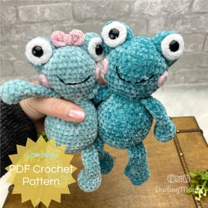 May include: Two crocheted teal green frog plushies with black eyes and pink cheeks. The smaller frog has a pink bow on its head. The text "LOW SEW PDF Crochet Pattern" is on a yellow starburst.