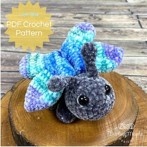 May include: A crocheted butterfly amigurumi toy with blue, purple and green wings and a grey body. The toy has large black eyes and is sitting on a wooden surface. The text "LOW SEW PDF Crochet Pattern" is visible in the image.