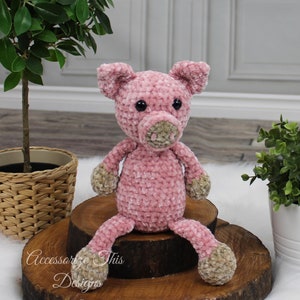 May include: A pink crocheted pig plush toy with brown felt accents for the nose and hooves. The pig is sitting on a wooden log slice.