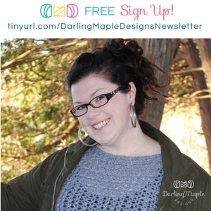 May include: A woman with dark hair and glasses smiles at the camera. She is wearing a blue knitted sweater with a lacy pattern, a green jacket, and large silver hoop earrings. The text "Darling Maple Designs" is visible in the lower right corner of the image.