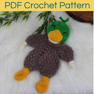 May include: A crocheted plush duck toy with a green head, brown body, and yellow feet. The duck has a white beak and a closed-eye expression.