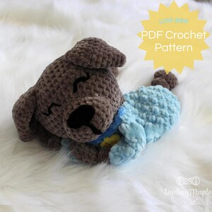 May include: A crocheted gray and blue dog plush toy laying on a white fluffy surface. The toy is wearing a blue and yellow crocheted blanket. The image includes the text "LOW SEW PDF Crochet Pattern".