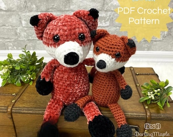 May include: A crochet pattern for making two plush fox toys. The pattern is available as a PDF download. The larger fox is red and the smaller fox is orange. Both foxes have black eyes and noses and white muzzles.