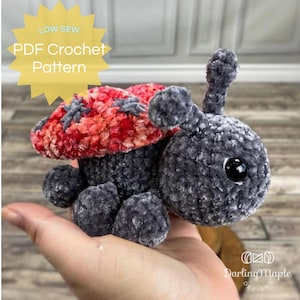 Könnte beinhalten: Ein Häkel-Amigurumi-Spielzeug in Form eines Marienkäfers mit einer rot-pinken Schale und einem grauen Körper. Das Spielzeug sitzt in der Hand einer Person. Das Bild enthält den Text "LOW SEW PDF Crochet Pattern" und "DarlingMaple Designs".